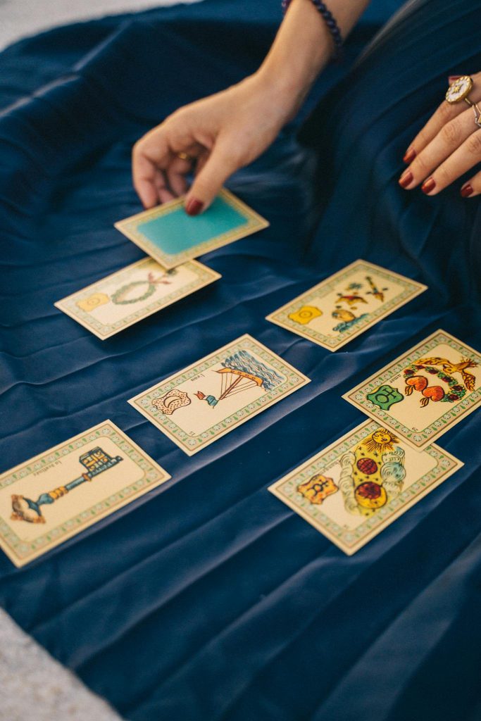 A close-up of tarot cards spread on a blue cloth with a hand selecting a card.